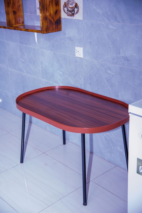 A wooden table with a red rim and black legs, positioned against a blue tiled wall with a white electrical outlet. - Dallas Style inner Apartment (Kigali)
