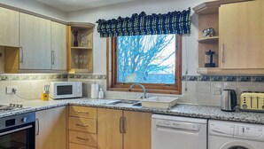 Une cuisine moderne avec des meubles en bois, un four à micro-ondes, un évier, un lave-vaisselle et une fenêtre donnant sur les arbres.