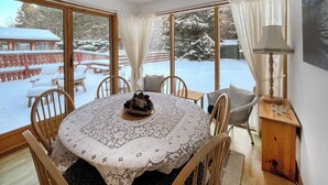 Un coin repas accueillant, avec une table dressée pour quatre personnes, entourée de chaises. De grandes fenêtres offrent une vue sur une terrasse enneigée à l’extérieur.