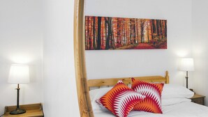 Un lit bien fait, avec une tête de lit en bois, deux tables de chevet avec des lampes et un tableau représentant une forêt accroché au mur.