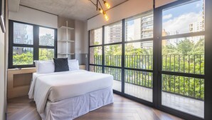 A modern bedroom with a large bed, built-in shelving, and large windows offering a view of the city. - Housi Faria Lima (São Paulo)