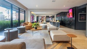 A modern hotel lobby with a reception desk, seating areas, and large windows offering views of the street. - Housi Faria Lima (São Paulo)