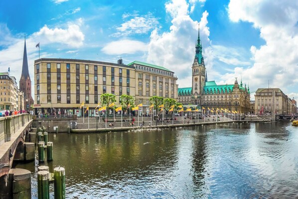 A riverside view with historic buildings, a prominent church spire, and a clock tower.