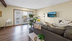 Ein Wohnzimmer mit grauem Sofa, einem weißen Sessel, einer Holzbank und einem Esstisch mit Pflanze.