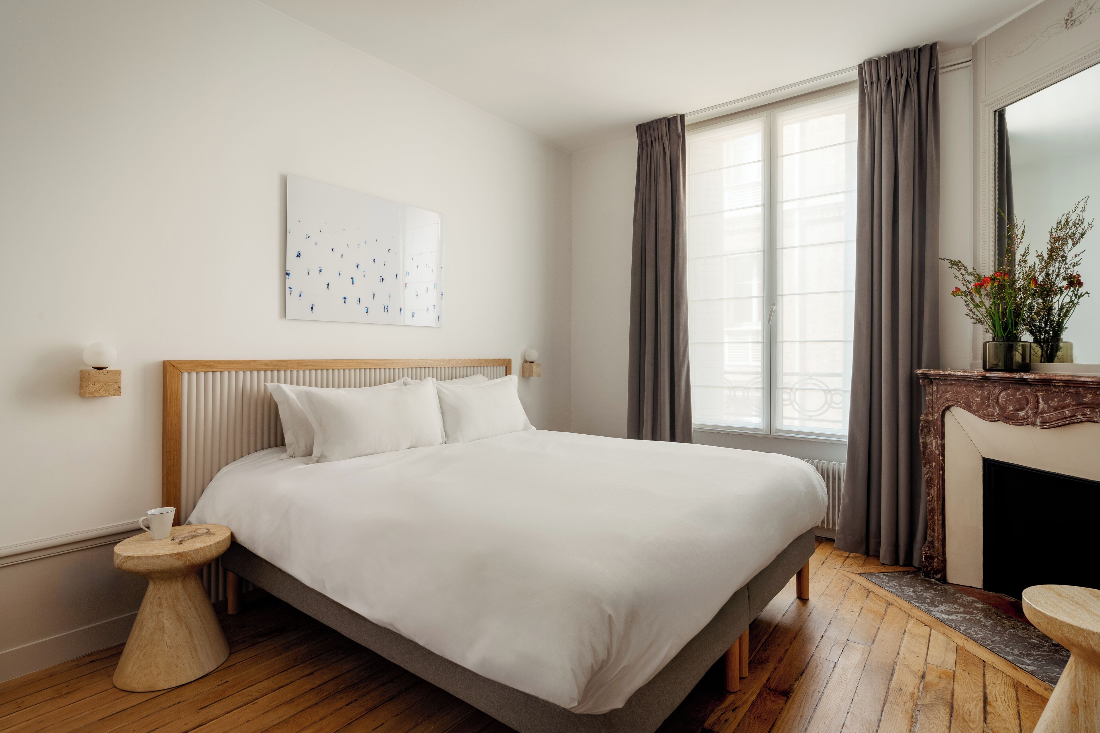 Ein ordentlich eingerichtetes Schlafzimmer mit einem großen Bett, einem kleinen runden Tisch, einem Kamin und einem Fenster mit Vorhängen.