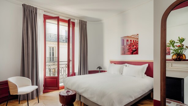 Ein Hotelzimmer mit einem großen Bett, einem Sessel, einem kleinen Tisch, einem Spiegel und Blick auf den Balkon.