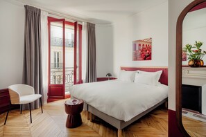 Ein Hotelzimmer mit einem großen Bett, einem Sessel, einem kleinen Tisch, einem Spiegel und Blick auf den Balkon.