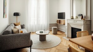 Ein Wohnzimmer mit einer Couch, einem runden Couchtisch, Kamin, Fernseher und einem Essbereich mit Stühlen.