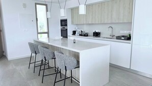 A modern kitchen with a central island, bar stools, a built-in oven, and a large window. - TooCoool Villa - Azure Seaview (Paralimni)