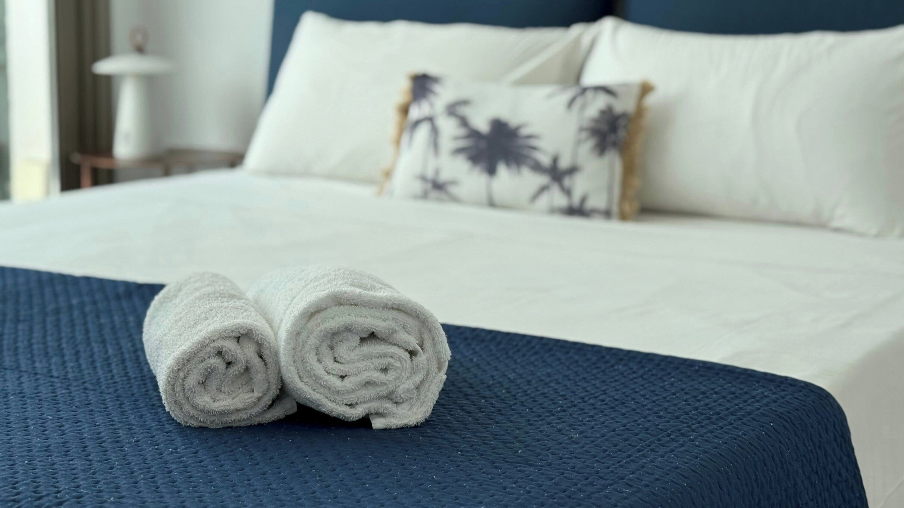 Ein ordentlich bezogenes Bett mit weißen Laken und einer blauen, strukturierten Tagesdecke.