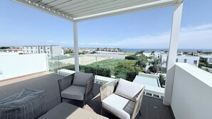 A balcony with a view of the sea and buildings, furnished with a sofa and chairs. - TooCoool Villa - Azure Seaview (Paralimni)