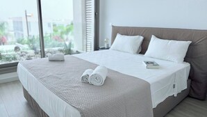A neatly made bed with white linens and a rolled towel, a book on the bed, and a view of greenery outside the window. - TooCoool Villa - Azure Seaview (Paralimni)