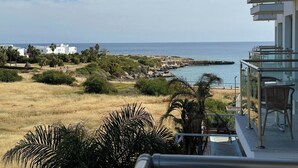 A balcony with a view of the sea, a grassy area, and some buildings in the distance.