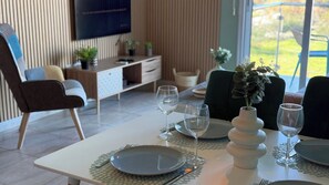 A dining area with a table set for two, two wine glasses, a vase with flowers, and a TV mounted on the wall.