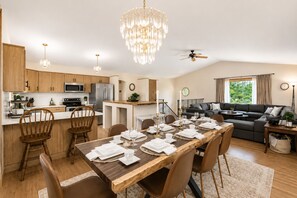 A modern kitchen with a dining area, a living room with a sofa and a coffee table, and a chandelier. - Whispering Pines Oasis 12 ac Scenic Forest Retreat (Amherst)