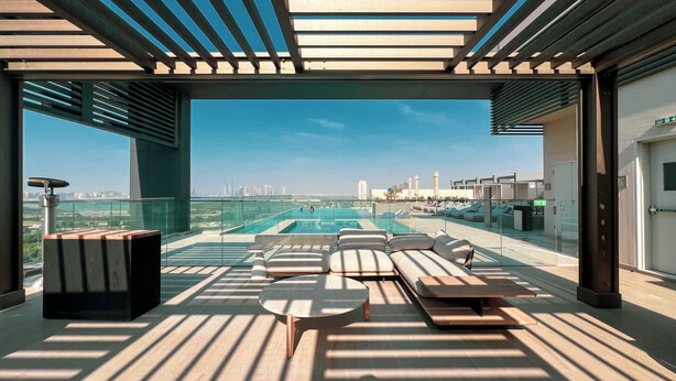Zona de piscina en la azotea con sillones de descanso, barandilla de cristal y vistas despejadas del horizonte urbano.