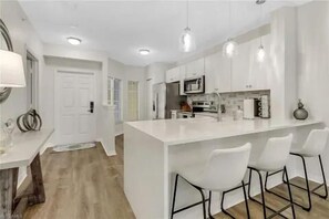 A modern kitchen with white cabinetry, a central island with bar stools, and pendant lighting.