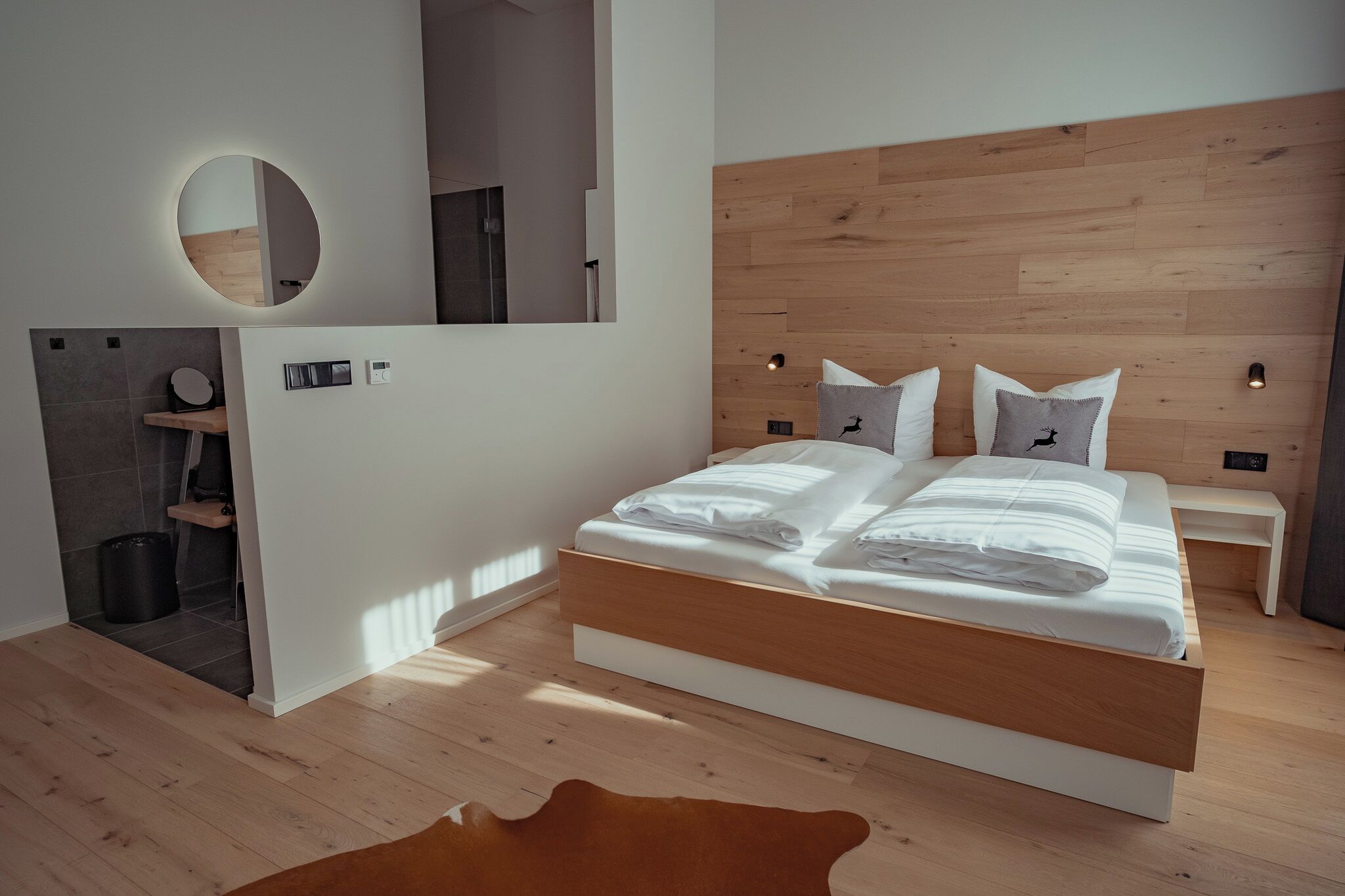 Un dormitorio moderno con cabecera de madera, un espejo redondo y una cama con ropa blanca.