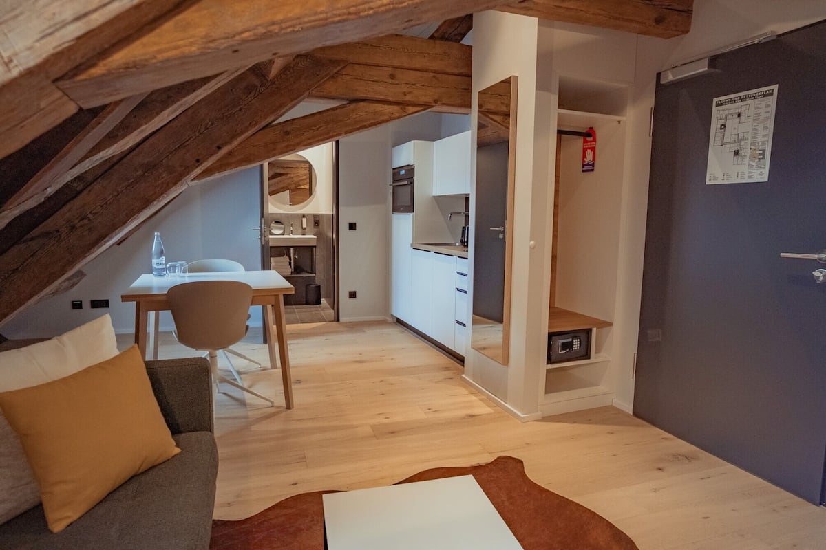 A cozy attic bedroom with a wooden ceiling, a dining area, and a kitchen.