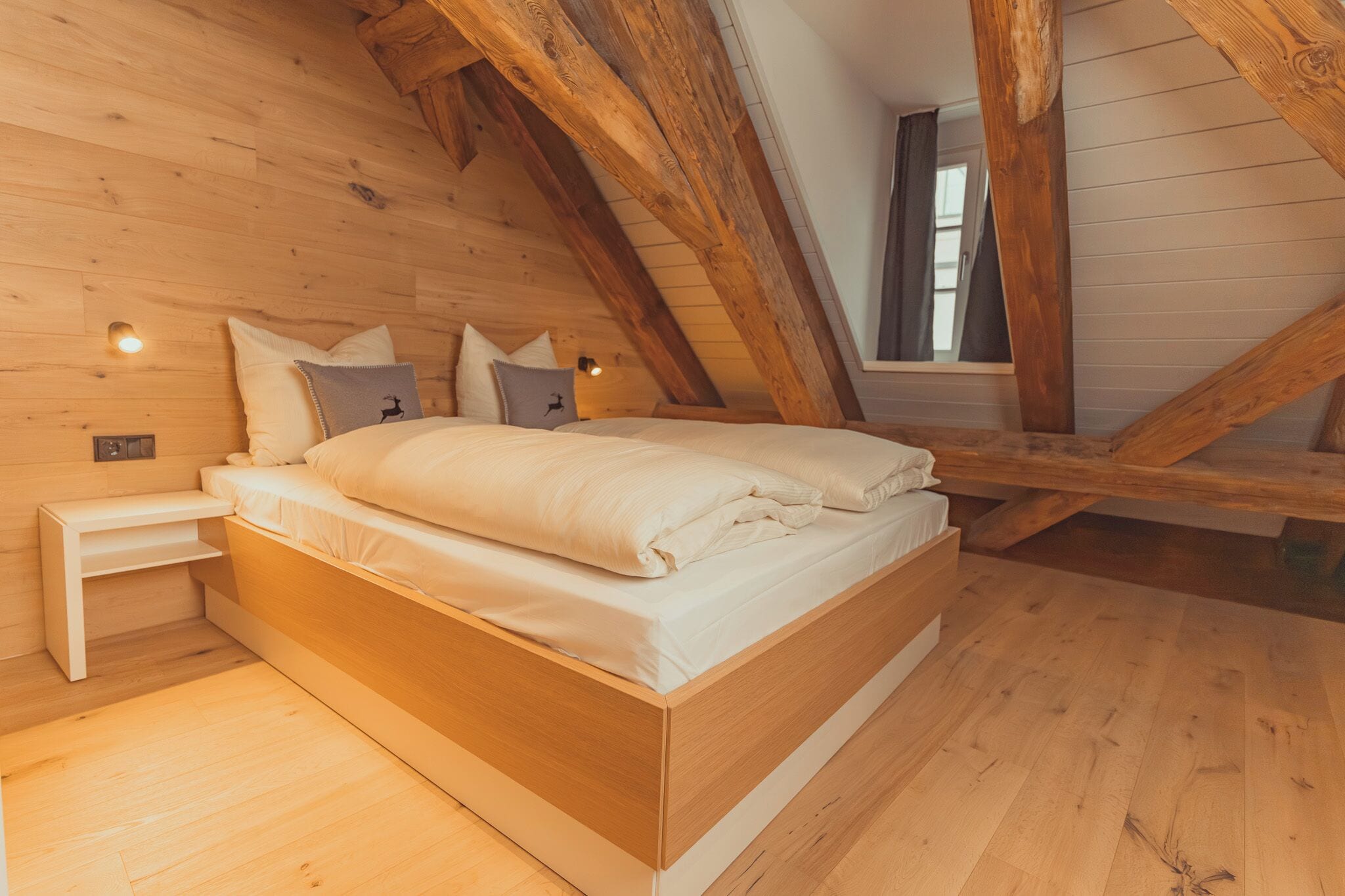A wooden-framed loft bedroom with a bed, bedside tables, and a window.