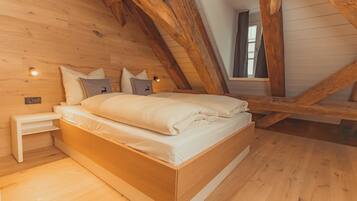 A wooden-framed loft bedroom with a bed, bedside tables, and a window.