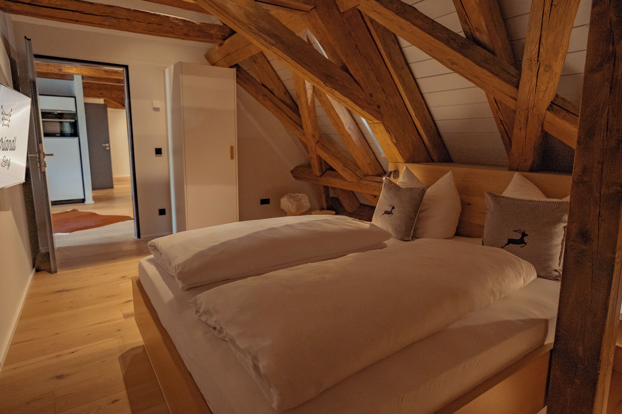 Un dormitorio con techo de madera, una cama con ropa de cama blanca y un almohadón con diseño de ciervo.