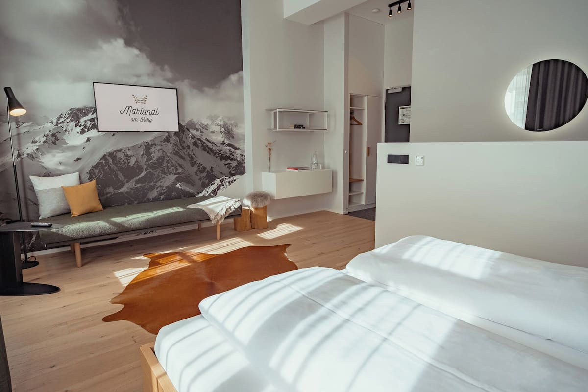 A modern bedroom with a mountain mural, a sofa, a cowhide rug, a bed, and a round mirror.