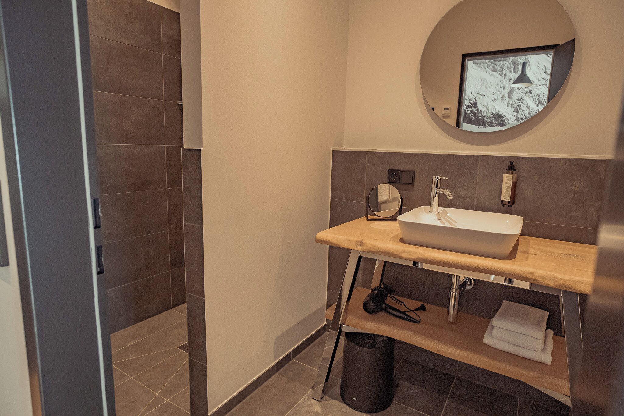 A modern bathroom with a wooden vanity, a round mirror, and a built-in sink.