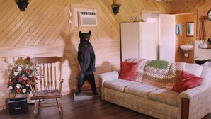 A wooden cabin interior with a bear statue, a sofa, a chair, and a small table with flowers. - Charming 2-bedroom cabin with AC, WiFi in brilliant Cisco Ga.  (Cisco)