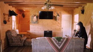 A cozy cabin interior with a wooden ceiling, a fireplace, a television, and mounted animal heads. - Charming 2-bedroom cabin with AC, WiFi in brilliant Cisco Ga.  (Cisco)