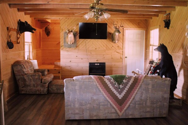 A cozy cabin interior with a wooden ceiling, a fireplace, a television, and mounted animal heads. - Charming 2-bedroom cabin with AC, WiFi in brilliant Cisco Ga.  (Cisco)
