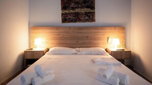A hotel room with a wooden headboard, two bedside lamps, a bed with white linens, and a painting on the wall. - Balcony Studio • Outdoor Kitchen • Uji i Ftohtë (Vlora)