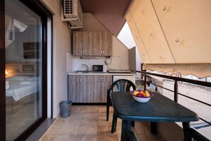 A balcony with a table, a bowl of fruit, a small kitchen area, and a view of the room.