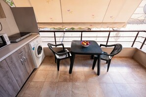 Une petite cuisine équipée d’un lave-linge, d’un four à micro-ondes, d’une table avec des chaises et d’un saladier rempli de fruits.