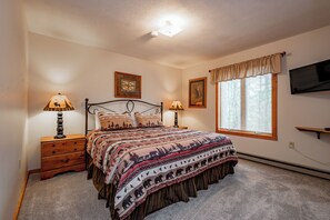 A bedroom with a bed, two bedside tables with lamps, a window with blinds, and a wall-mounted TV. - Tranquil Lake Retreat w/ Hot Tub & Games (Oakland)