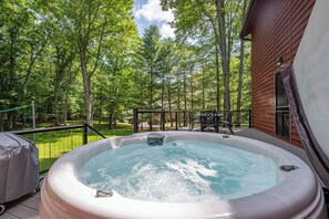 A hot tub on a deck with a view of a forest and a building.