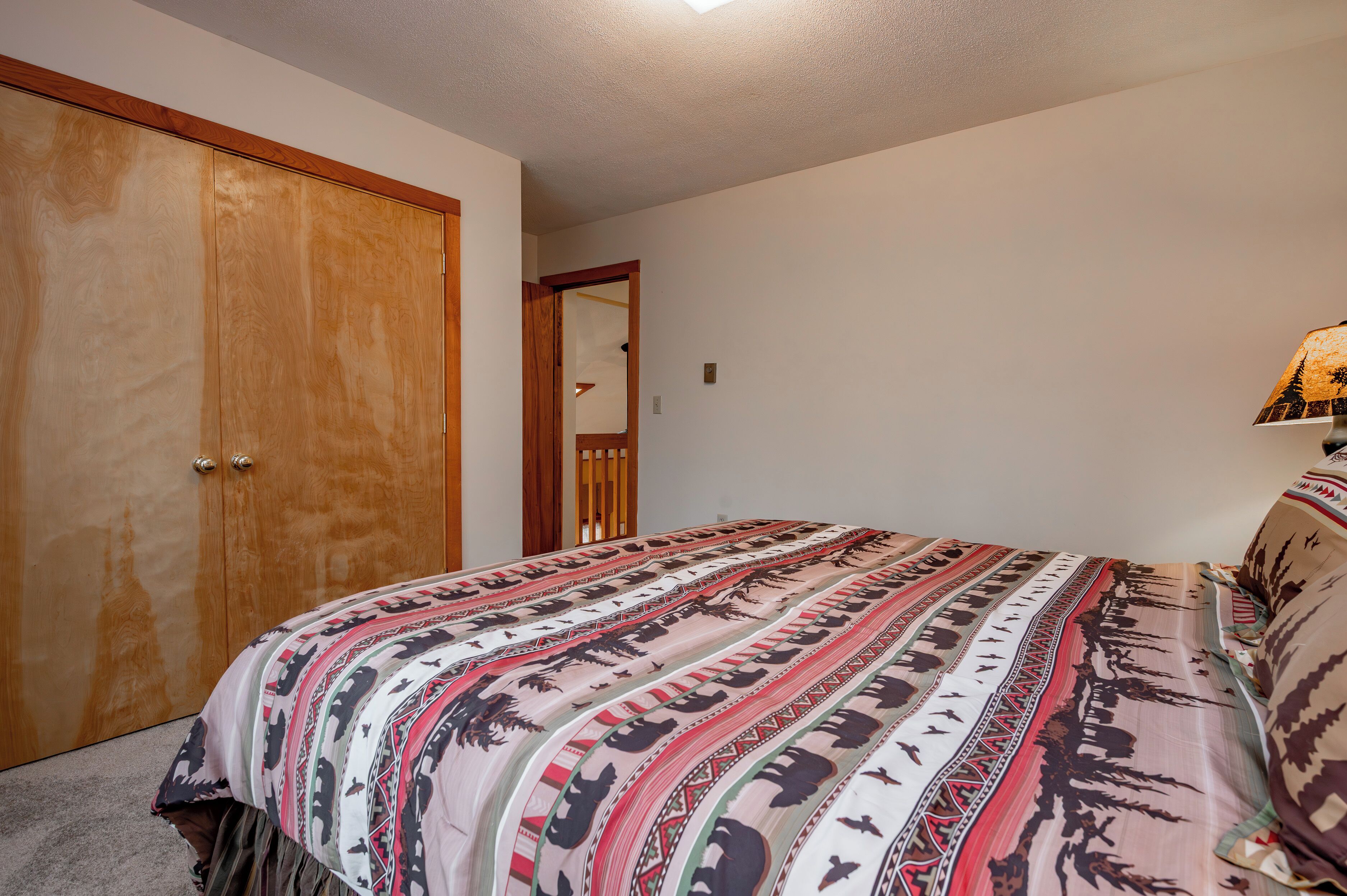 A bedroom with a large wooden wardrobe, a bed with a patterned bedspread, and a bedside lamp.
