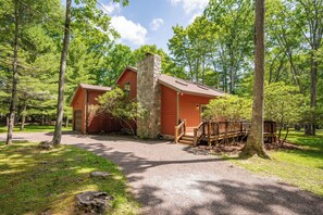 A cabin with a stone chimney, surrounded by trees, and accessible by a gravel path.