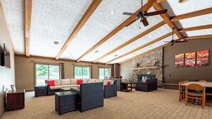 A spacious living area with a high ceiling, wooden beams, and a stone fireplace. There are multiple seating options including a sofa and chairs, and a dining table with chairs.