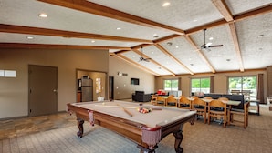 A spacious indoor area with a pool table, wooden ceiling beams, and a seating area with tables and chairs.