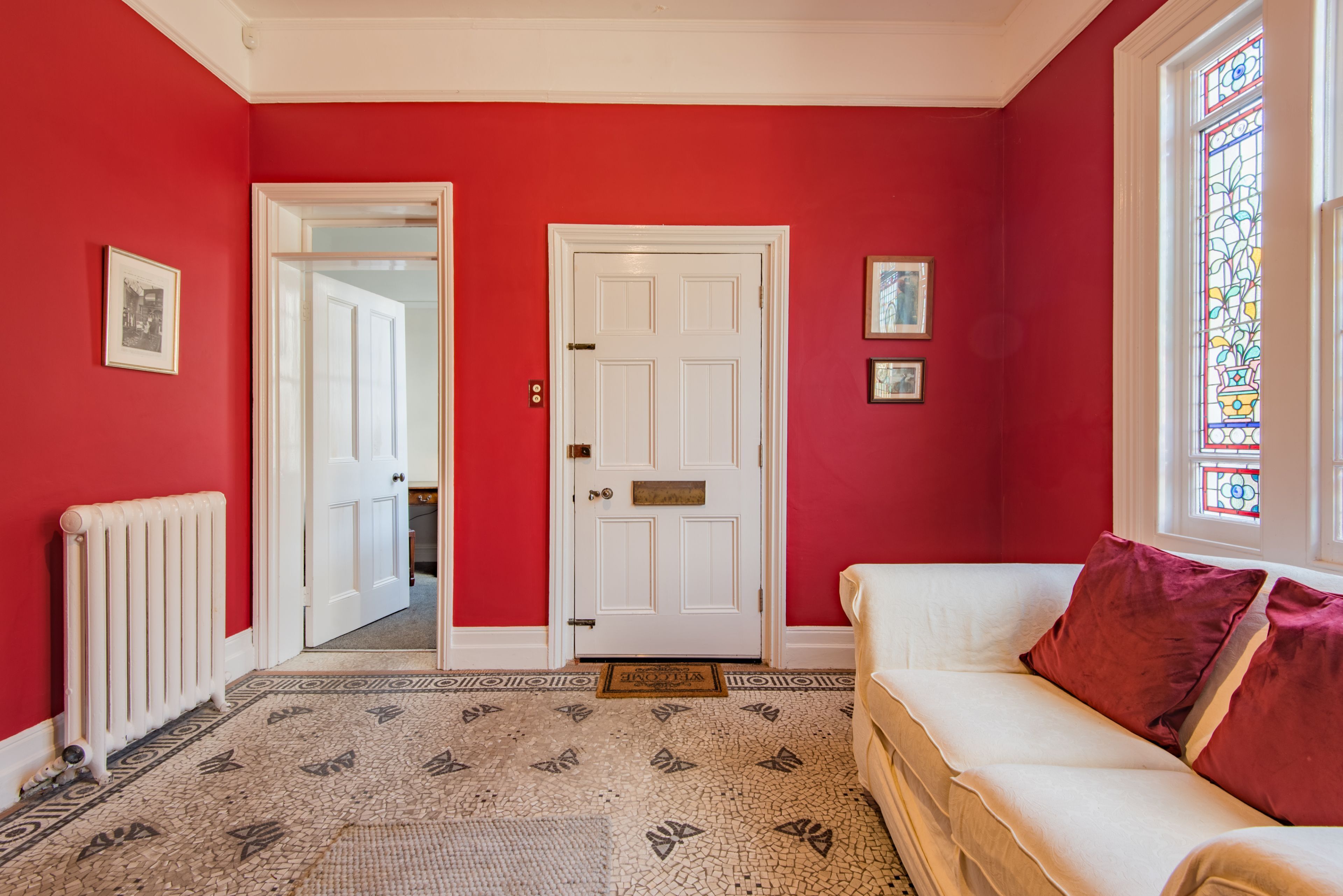 A hallway with a red wall, a white door, and a white sofa with red cushions.