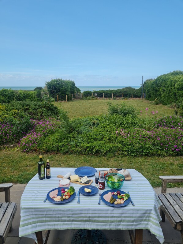 A table set outdoors with food and drinks, surrounded by greenery and a view of the sea.