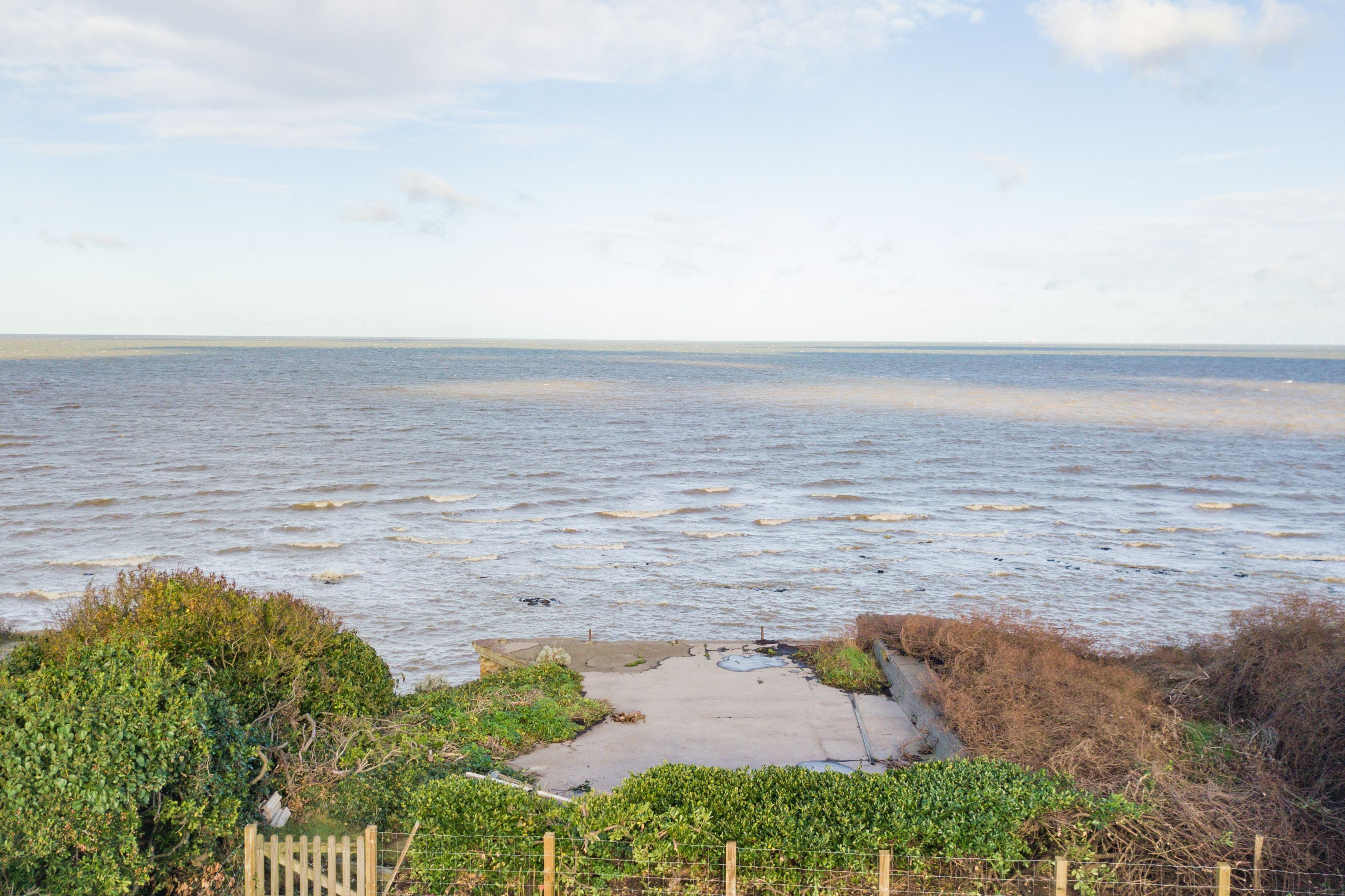 Une vue sur la côte, avec une plage de sable, une clôture en bois et une végétation luxuriante.
