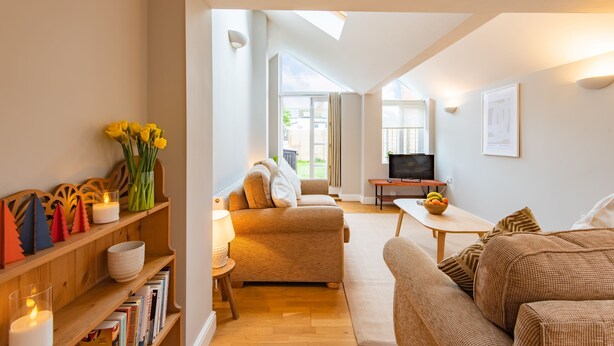 A modern living room with a sofa, a coffee table, and a television. There is a bookshelf with books and decorative items.