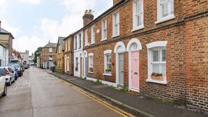 A row of traditional brick houses with distinct door numbers, parked cars on the street, and a clear sky.