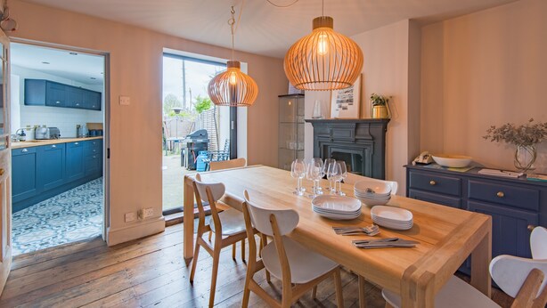 A dining area with a wooden table set for six, surrounded by chairs, and two pendant lights hanging above. - Seaclusion - Walmer, Deal (Walmer)