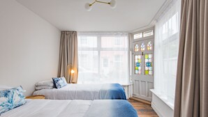 A hotel room with two beds, a window with curtains, a wall-mounted light, and a stained glass window. - Seaclusion - Walmer, Deal (Walmer)