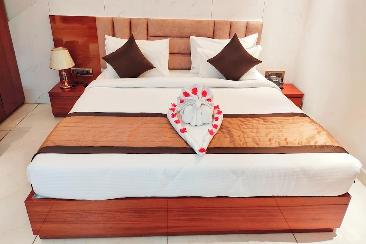 Een net opgemaakt bed met een hartvormig sierkussen, een houten hoofdbord en een nachtkastje met een lamp.