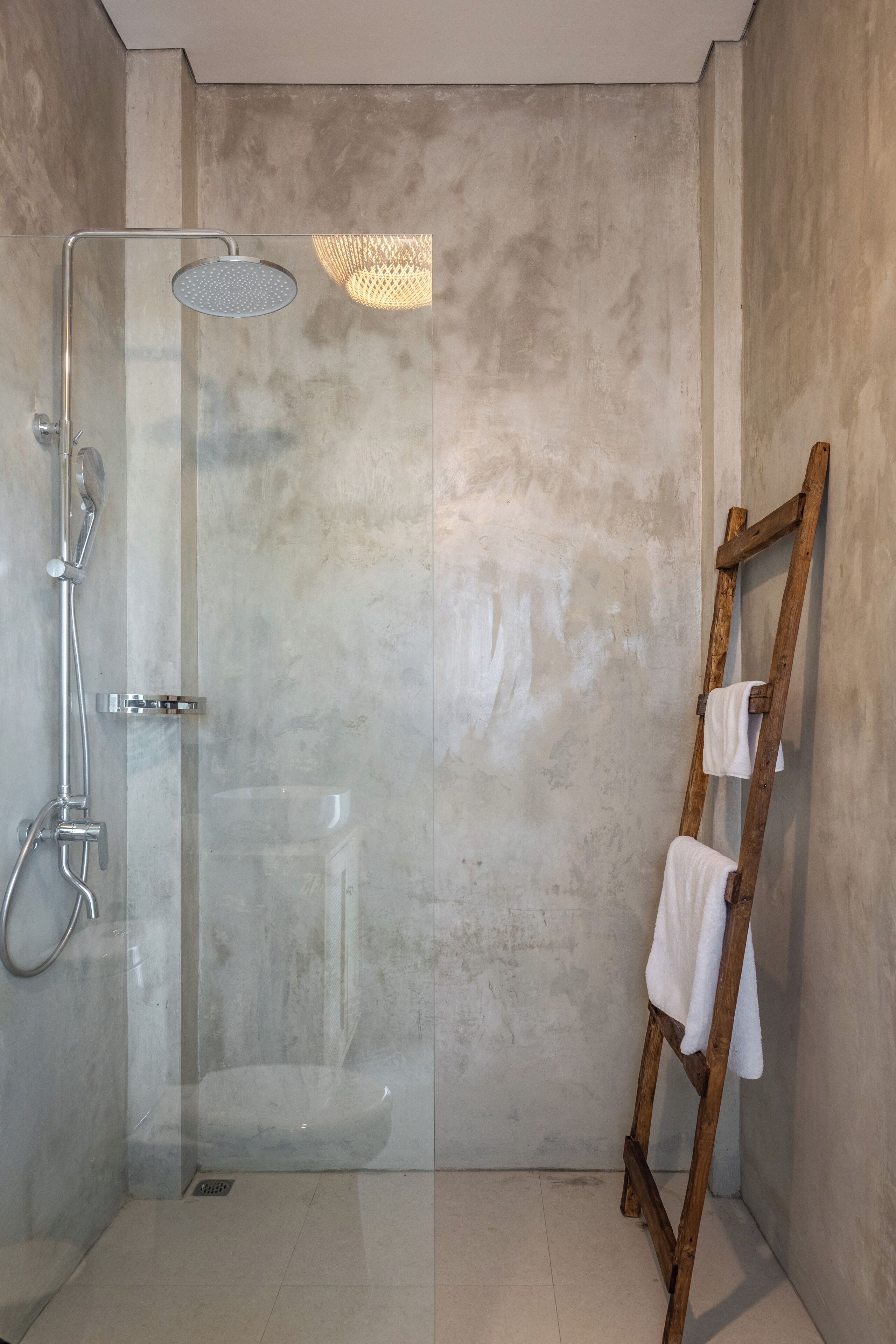 A modern bathroom with a glass-enclosed shower, a wooden ladder with towels, and a textured wall.