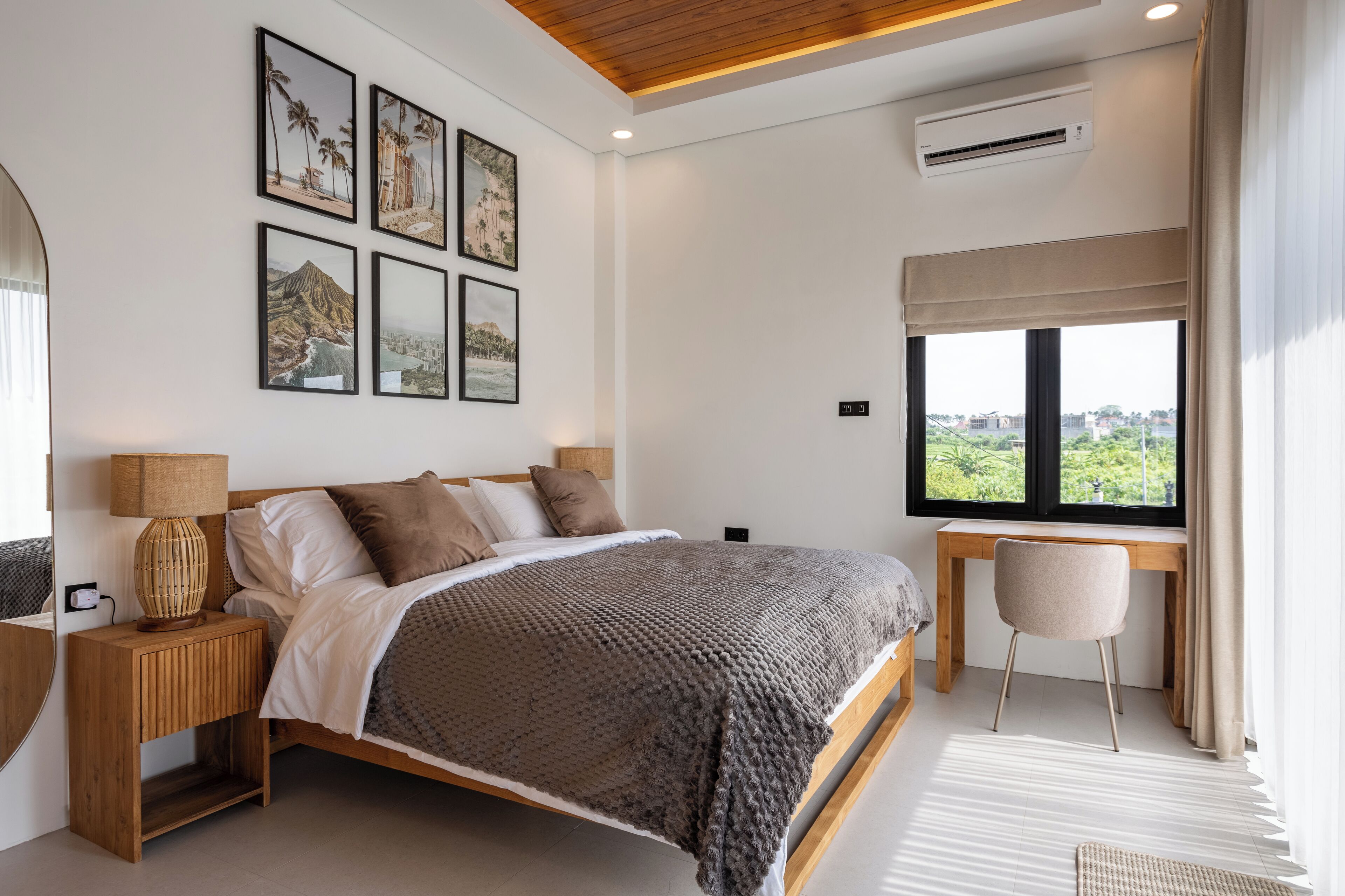 A bedroom with a bed, bedside table, lamp, and a desk with a chair. There are four framed pictures on the wall.
